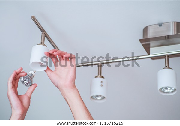 Replacing a burned-out halogen lamp in the soffit.\
The man holds the lampshade with one hand and inserts the lamp into\
the base with the\
other.