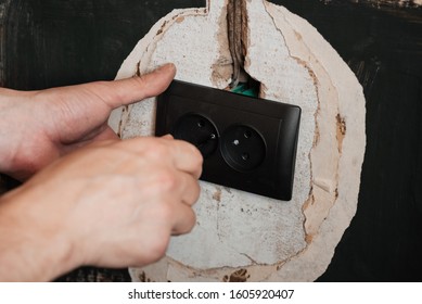 Replacing and installing a new electrical outlet. Hands with a screwdriver male electrician on the background of the wall in the house making repairs to the socket