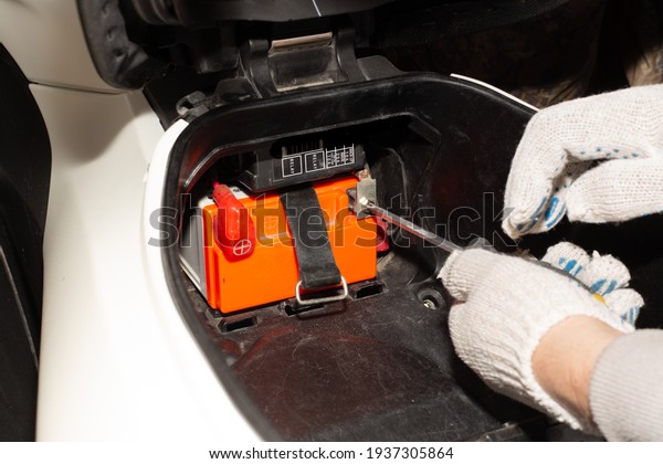 Replacing the motorcycle battery. An auto\
mechanic in a car service uses a screwdriver to remove the battery\
from the motorcycle to charge or replace\
it.