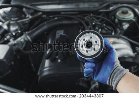 Replacing the oil filter. Car engine maintenance mechanic holds an oil filter in his hand against the background of an open car hood