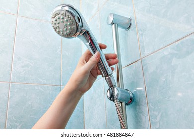 Replacing the plumbing in the bathroom, close-up wall mounted hand shower and hose holder with height adjustable bar slider rail, human hand holding a shower head.
