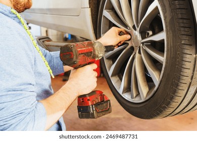 Replacing summer tires for winter using pneumatic wrench tool by mechanic worker after balancing wheels in car service garage shop