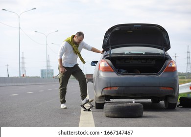 Replacing The Wheel Of A Car On The Road. A Man Doing Tire Work On Sidelines.