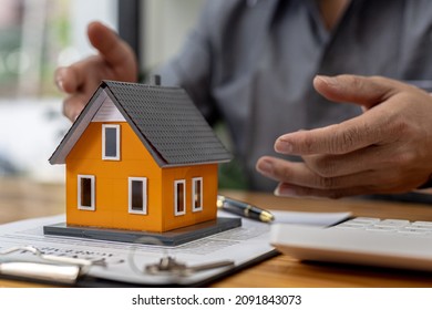 Replica of a small orange house sits on a table, a housing project salesperson is drafting a sales contract for a customer who reserves a house in the project he maintains. Real estate trading concept - Shutterstock ID 2091843073