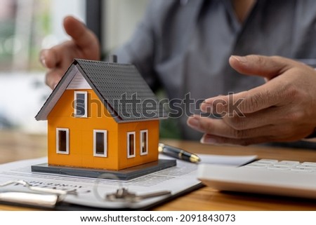 Replica of a small orange house sits on a table, a housing project salesperson is drafting a sales contract for a customer who reserves a house in the project he maintains. Real estate trading concept 商業照片 © 