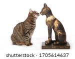 
replica of a statue of the Egyptian cat goddess Bastet in front of a real European tabby cat as comparison on studio isolated white background