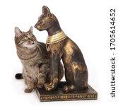 
replica of a statue of the Egyptian cat goddess Bastet in front of a real European tabby cat as comparison on studio isolated white background