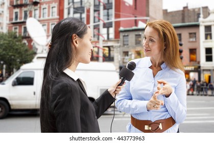 A Reporter With A Microphone Interviews A Woman In New York City With A News Van In The Background.