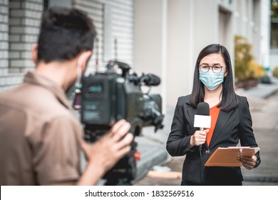 Reporter woman holding a microphone with reporting news and cameraman shooting outdoor news update while wearing  mask prevent Covid-19 or coronavirus quarantine pandemic.