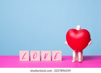 Representation of love on a special day: wooden doll sitting with a huge heart next to the word love - Shutterstock ID 2257896559