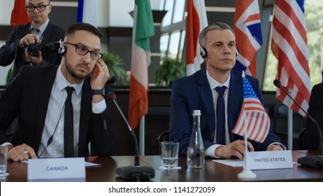Representative men of different countries sitting at table on conference and listening to speech interpretation in headphones