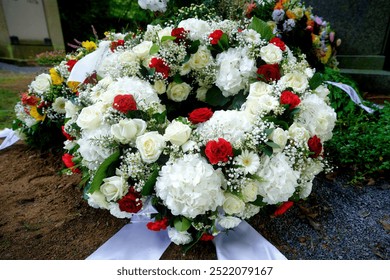 Representative white funeral wreath of hydrangeas, roses, daisies, gypsophila and some red roses on a grave after a funeral