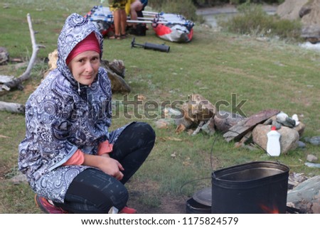 the Republic of Altai, Russia. A young tourist is preparing a camp dinner. Cute active girl in the mountains in the campaign.