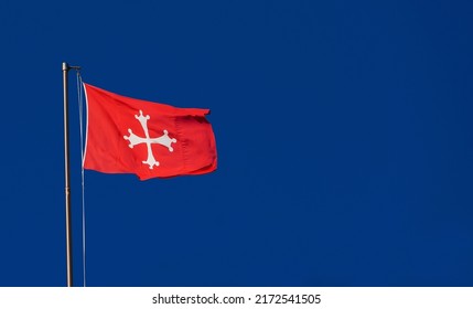 Republic of Pisa old red flag with white cross waving in the wind. One of the most powerful ancient Maritime Republic in the Mediterranean Sea during the Middle Ages (with blue sky and copy space)