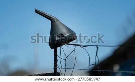 Repurposed plastic funnel attached to a barbed wire fence against a clear blue sky, demonstrating recycling and ingenuity