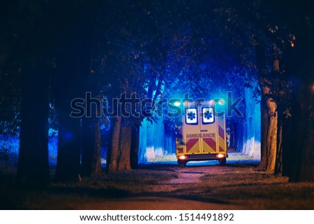 Rescue in dark alley. Rear view of ambulance of emergency medical service against illuminated trees from blue flasher.