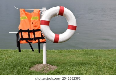 rescue equipment, life jacket and lifebuoy hanging on metal post waterfront lawn, safety device for water activities - Powered by Shutterstock