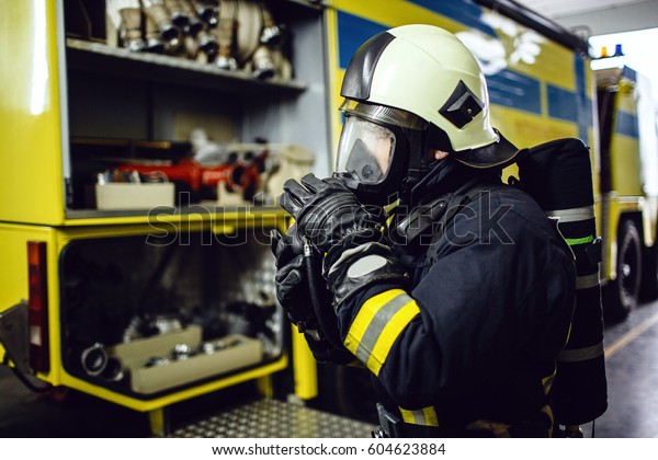Rescue firefighter in safe helmet and uniform\
standing by car
