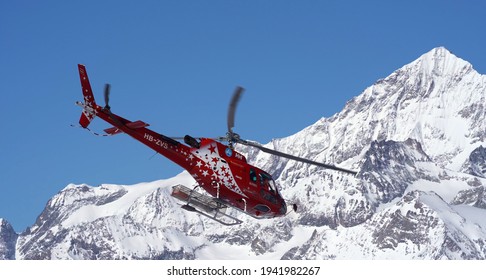 Rescue Helicopter Of Air Zermatt With Snow Capped Mountains In The Background On A Sunny Spring Day. Photo Taken March 23rd, 2021, Gornergrat, Zermatt, Switzerland.