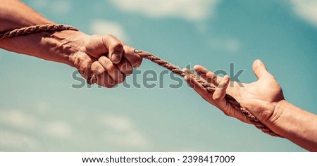 Rescue, help, helping gesture or hands. Conflict tug of war. Rope, cord. Hand holding a rope, climbing rope, strength and determination. Strong hold. Two hands, helping hand of a friend.