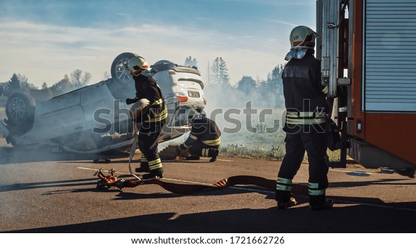 Rescue Team of Firefighters Arrive at the Crash,
Catastrophe, Fire Site on their Fire Engine. Firemen Grab their
Equipment, Prepare Fire Hoses and Gear from Fire Truck, Rush to
Help Injured People.