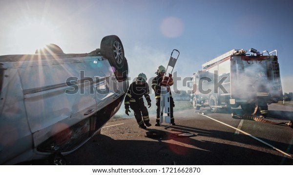 Rescue Team of Firefighters Arrive on Car Crash
Traffic Accident Scene on their Fire Engine. Firemen Grab their
Equipment, Prepare Fire Hoses and Gear from Fire Truck, Rush to
Rescue Injured People