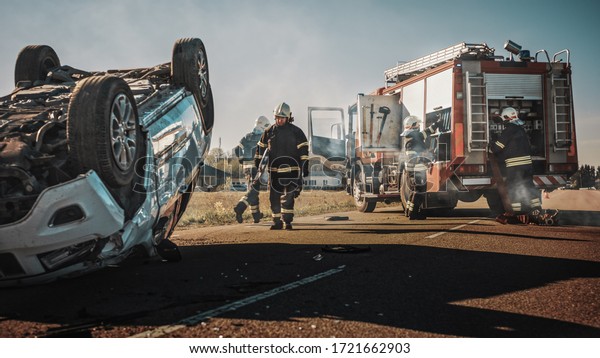 Rescue Team of Firefighters Arrive on the Car
Crash Traffic Accident Scene on their Fire Engine. Firemen Grab
their Tools, Equipment and, Gear from Fire Truck, Rush to Help
Injured, Trapped People