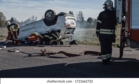 Rescue Team Of Firefighters And Paramedics Work On A Terrible Car Crash Traffic Accident Scene. Preparing Equipment, Stretches, First Aid. Saving Injured And Trapped People From The Burning Vehicle