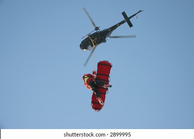 A Rescue Worker Flies Under A Helicopter With A Patient In A Rescue Stretcher.