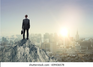 Research concept with businessman standing on mountain top and looking at sun setting over city - Shutterstock ID 439436578