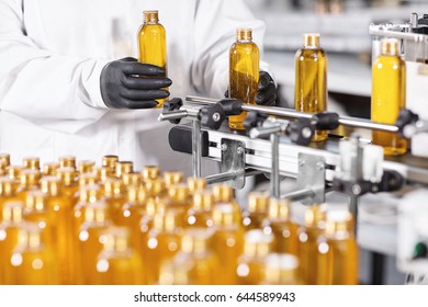 Research and development concept. Hands of professional worker of factory putting glass bottles with yellow liquid on conveyor line. Automated process of producing cosmetic products on factory