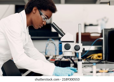 Research And Development Of Electronic Devices By Black Woman. Scientist African American Woman In Gloves Working In Laboratory With Electronic Tech Instruments And Microscope.