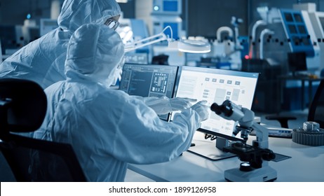 Research Factory Cleanroom: Engineer and Scientist Wearing Coveralls Talk and Work on Computer, Use Microscope to Inspect Motherboard Microprocessor, Develop Electronics for Medical Electronics - Powered by Shutterstock