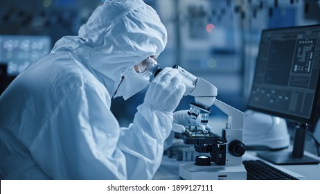 Research Factory Cleanroom: Engineer Scientist wearing Coverall, Gloves Uses Microscope to Inspect Samples, Developing High Tech Modern Technology for Medical and High Precision Electronics Industry