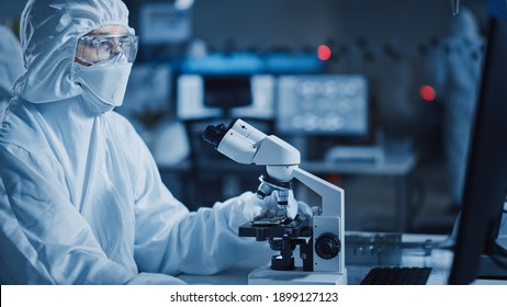 Research Factory Cleanroom: Engineer Scientist Wearing Coverall And Uses Microscope To Inspect Samples, Developing High Tech Modern Technology For Medical And High Precision Electronics Industry