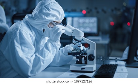 Research Factory Cleanroom: Engineer Scientist Wearing Coverall, Gloves Uses Microscope To Inspect Samples, Developing High Tech Modern Technology For Medical And High Precision Electronics Industry