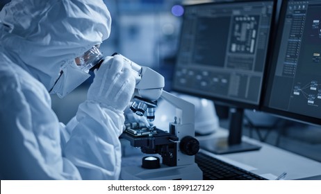 Research Factory Cleanroom: Engineer Scientist Wearing Coverall And Uses Microscope To Inspect Samples, Developing High Tech Modern Technology For Medical And High Precision Electronics Industry