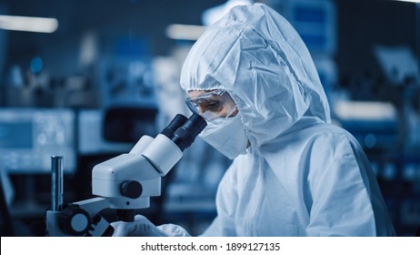 Research Factory Cleanroom: Engineer Scientist wearing Coverall and Uses Microscope to Inspect Samples, Developing High Tech Modern Electronics for Medical and High Precision Electronics Industry