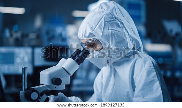 Research Factory Cleanroom: Engineer Scientist\
wearing Coverall and Uses Microscope to Inspect Samples, Developing\
High Tech Modern Electronics for Medical and High Precision\
Electronics Industry