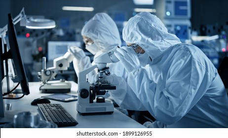 Research Factory Cleanroom: Engineers Scientists wearing Coveralls and Gloves Use Microscopes to Inspect Motherboard Microprocessor Components, Developing High Tech Modern Electronics