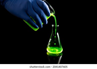 A research scientist experimenting with a green fluorescent droplets in a glass conical flask in dark biomedical laboratory for health care medicine development. Copy space black background