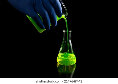 A Research Scientist Experimenting With A Green Fluorescent Droplets In A Glass Conical Flask In Dark Biomedical Laboratory For Health Care Medicine Development. Copy Space Black Background