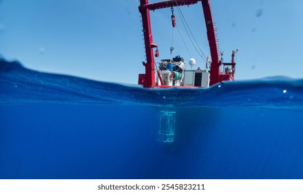 A research vessel floats over the deep blue ocean with submerged equipment prepared for scientific exploration. - Powered by Shutterstock