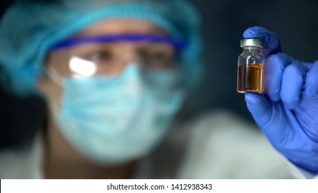 Researcher analyzing transparent brownish liquid in bottle, antidote development - Shutterstock ID 1412938343