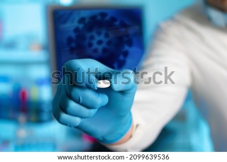 Researcher with antiviral pill drugs against covid-19 in front of an illustration of coronavirus. Doctor hand giving antiviral pills for medication of patients of covid-19 coronavirus