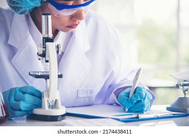 Researcher Biology Chemistry. Asian Female Technician Laboratory Using Microscope Blood Test. Asian Woman Scientist Hand Write Note Research In Medical Lab Look At Science Microscope Medical Test