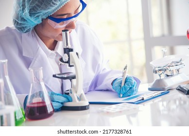 Researcher Biology Chemistry. Asian Female Technician Laboratory Using Microscope Blood Test. Asian Woman Scientist Hand Write Note Research In Medical Lab Look At Science Microscope Medical Test