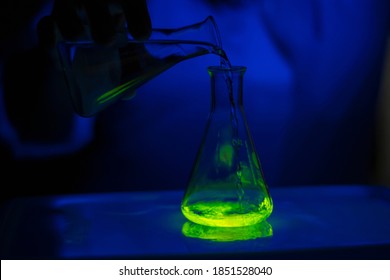 A researcher experimenting with a green fluorescent compound in a glass conical flask in dark biochemistry laboratory for health care development