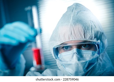 Researcher In Hazmat Protective Suit Examining A Test Tube In The Chemical Lab.