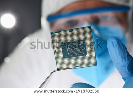 Researcher holds small microcircuit with tongs. Chipping and microcircuits concept